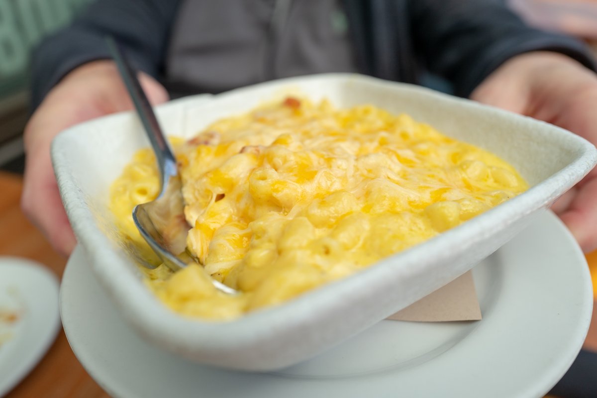 Close-up of plate of Peruvian macaroni and cheese with bacon, with mans hands visible in background, at Parada restaurant in Walnut Creek, California, March 4, 2021.